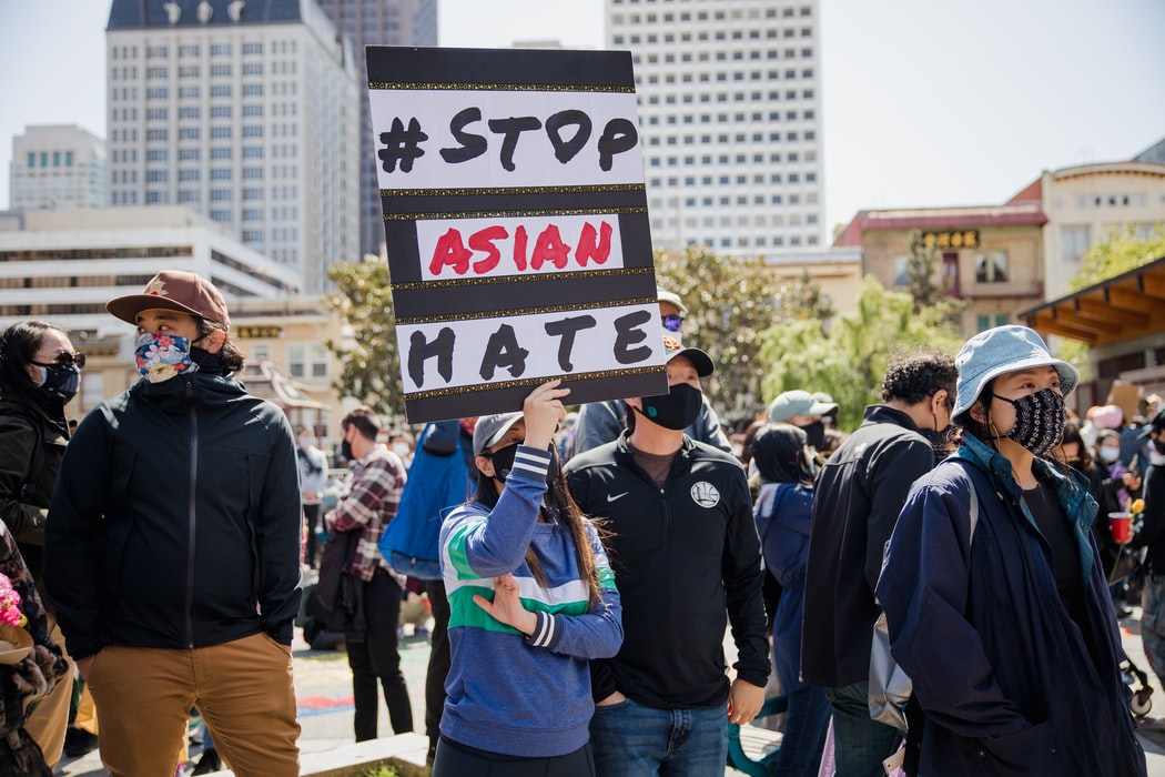 photo in a crowd, woman holding up sign that reads "#stop asian hate"