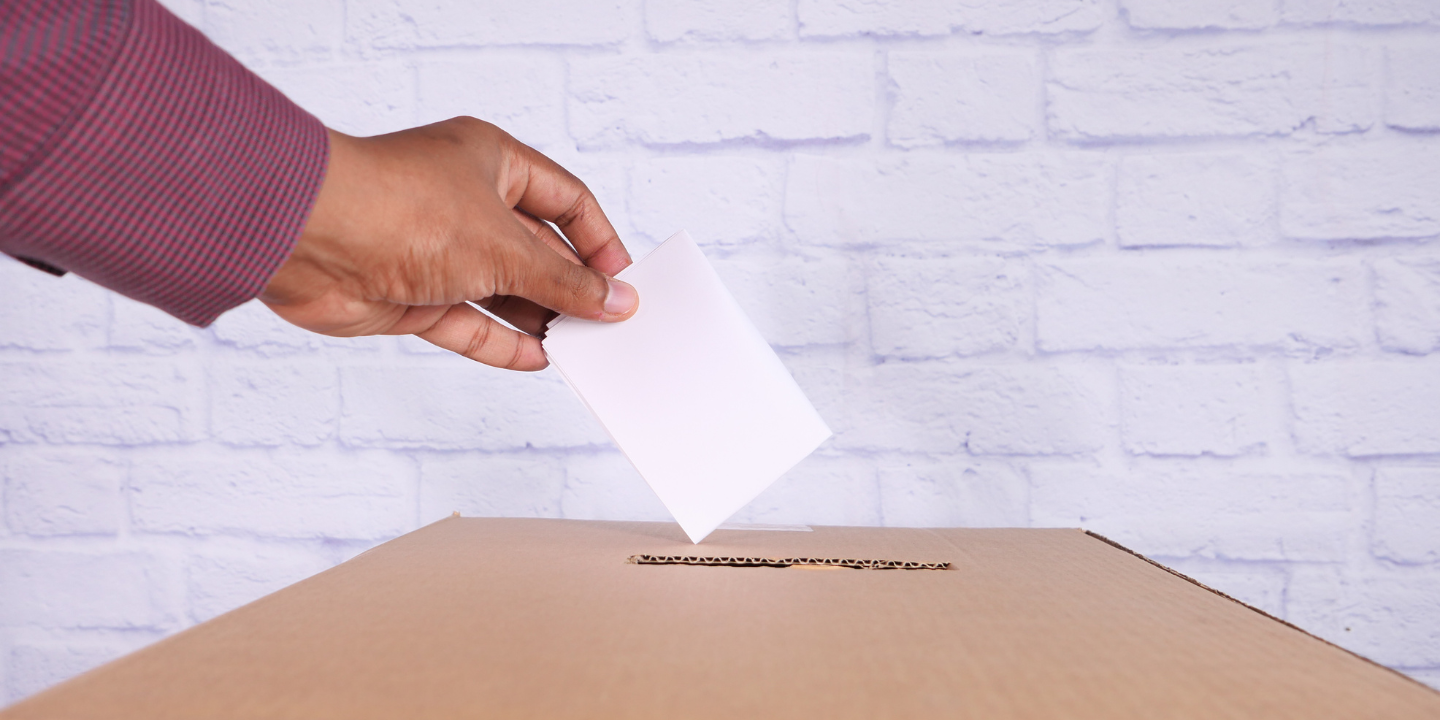A hand putting a ballot into a ballot box
