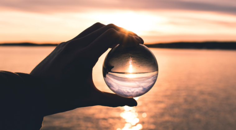 Hand holding a glass see through ball against a sunset over water