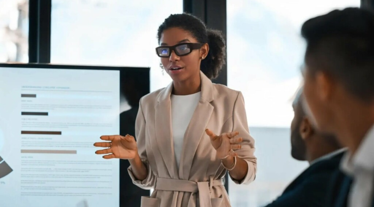 Business leader wearing AI smart glasses presenting during a workplace meeting discussing technology and collaboration